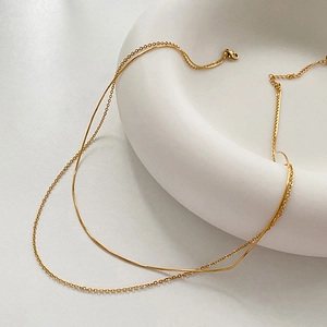 Detailed close-up of golden double-layer necklace featuring snake and cross chains