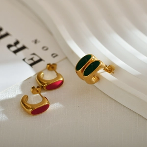 Elegant gold-plated geometric stud earrings with red and green enamel on a wavy stand