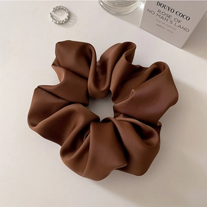 Detailed close-up of a large satin scrunchie in caramel brown on a minimal white background