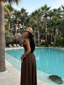 Elegant brown sleeveless off-shoulder long dress with pleats by the resort pool
