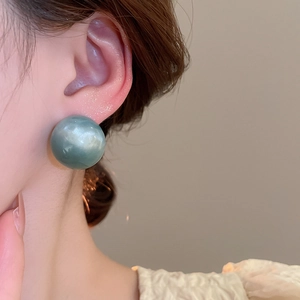 Detail view of a large round dark green earring with a smooth glossy resin finish