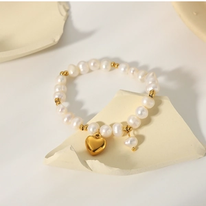 Macro detail of French freshwater pearls and gold heart pendant on titanium steel bracelet