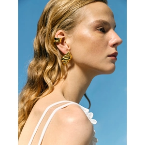 Golden seashell ocean wave earring and ear cuff set worn by model against blue sky