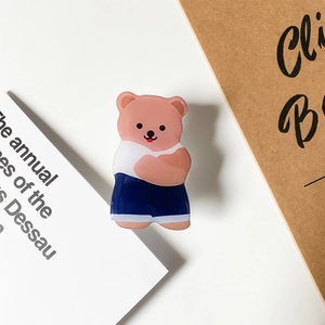 Close-up of cute cartoon bear acrylic phone grip with blue shorts on white desk