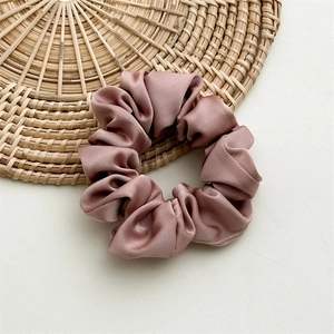 Detail of dusty rose satin scrunchie showing smooth silk texture and pleats on woven mat