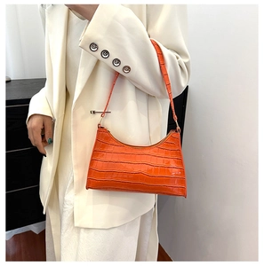 Detail of orange crocodile pattern underarm bag on a model wearing a white suit