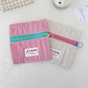 Detail of pink and beige pleated cosmetic bags with contrasting zippers and brand labels