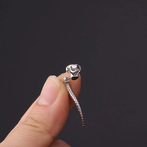 Detailed macro of a silver snake cartilage earring with tiny pink gemstone eyes