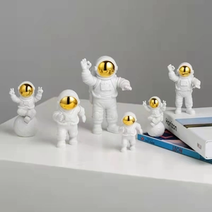 Set of six white and gold astronaut figurines displayed on decorative books and stand