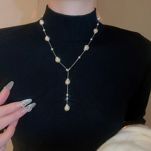 Detailed view of gold-plated Y-shaped necklace with baroque pearls on black sweater