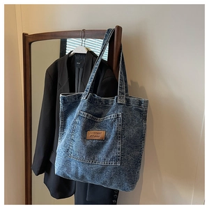 Detail of vintage washed blue denim tote bag with leather logo tag and front pocket