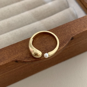 Close-up of gold-plated open ring with white pearl and teardrop metal detail