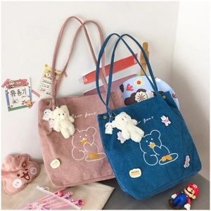 Detail of corduroy tote bags in pink and blue featuring cute bear embroidery and charms