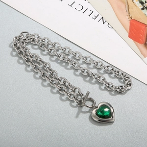 Collier chaîne argentée avec pendentif cœur en cristal vert et fermoir OT sur fond marbre