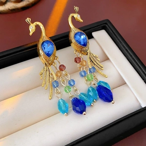 Detail of vintage gold peacock earrings with blue stones and colorful beaded tassels