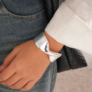 Close-up of polished silver twisted cuff bracelet styled with denim and white linen