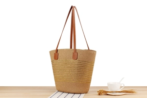Detail of woven straw tote bag with golden stripes and brown leather handles