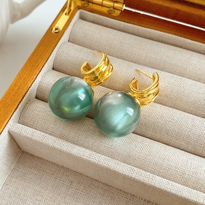 Detailed close-up of green resin sphere drop earrings resting in a beige jewelry box