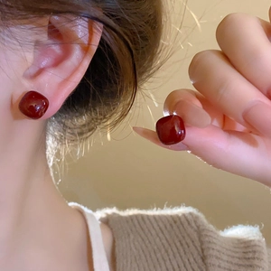 Close-up of red square stud earring with glossy finish worn by a model in soft light