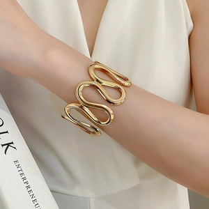 Detailed view of wide gold irregular wave cuff bracelet worn with modern fashion attire