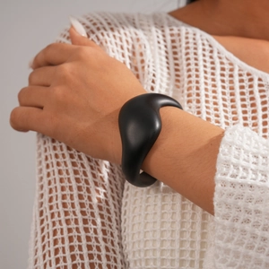 Close-up of matte black irregular geometric bangle on model's wrist with mesh fabric