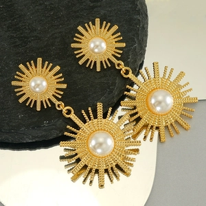 Golden sunburst drop earrings with pearls on black rock with mirror reflection