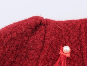 Dettaglio macro del cardigan rosso con perla finta, nastro e decorazioni in piuma