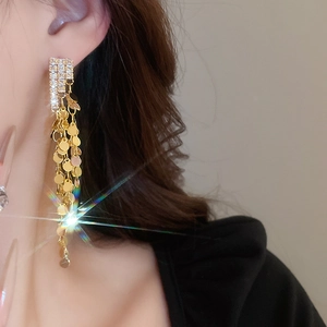 Detailed view of long gold tassel earrings with sequins and sparkling rhinestones