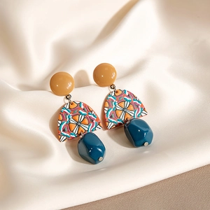Close-up of yellow and blue acrylic geometric drop earrings on white silk fabric