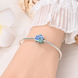 Detail of silver snake chain bracelet with blue enamel charm on a model's wrist