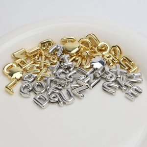 18k gold and silver bubble letter charms and heart pendant in a white ceramic dish