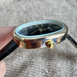 Close-up of golden oval watch case and crown with black leather strap detail