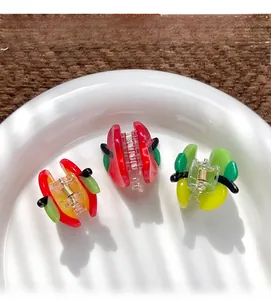 Detailed view of small fruit-shaped hair claws with golden springs on a ceramic plate