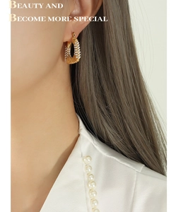 Detail of U-shaped gold plated titanium earrings with small pearls on female model