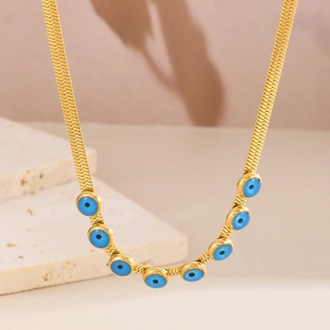 Golden snake chain necklace with blue evil eye charms on a soft neutral background