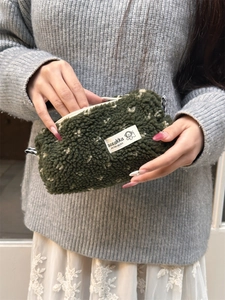 Close-up of plush dark green heart pencil case with soft texture and brand label