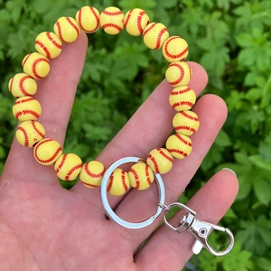 Hand holding a yellow softball beaded keychain wristlet with silver metal hardware detail