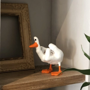 Detail of a funny white resin duck figurine with middle finger gesture on a wooden shelf