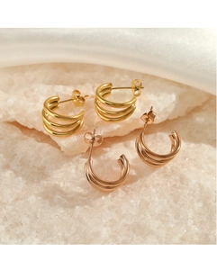Macro shot of three-layer C-shaped earrings in polished gold and rose gold on white stone