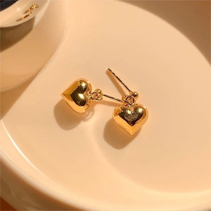 Macro shot of minimalist gold heart stud earrings on a cream ceramic surface