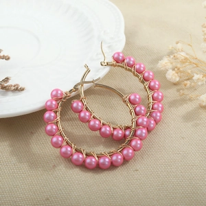 Close-up of gold hoop earrings with handmade pink pearl beading on textured linen