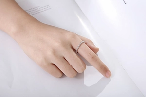 Detail of a thin silver twisted rope ring on a finger with a minimalist white book background