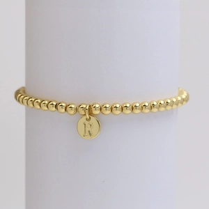 Detail of golden bead bracelet with an engraved letter R pendant on a white pedestal