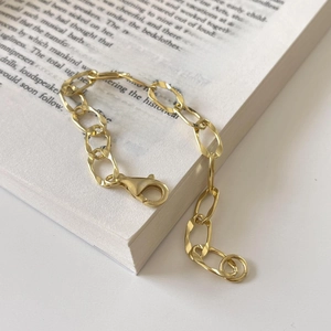 Detail of a polished gold oval link chain bracelet with a lobster clasp on a book