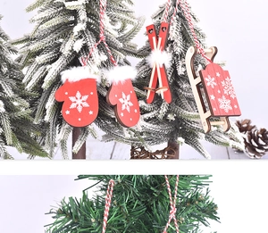 Detail of wooden Christmas ornaments featuring red gloves, skis and sled on snowy pine branches