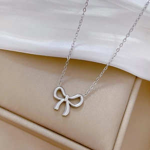 Close-up of a silver bow pendant necklace resting on a beige jewelry gift box