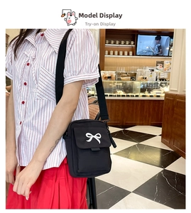 Close-up of a black canvas crossbody bag featuring a large white bow on a model