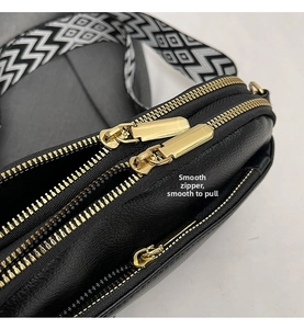 Detail of black lychee grain leather bag with triple gold zippers and patterned strap