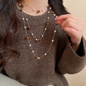 Elegante mehrlagige Tigerauge- und Perlenkette vor braunem Pulloverhintergrund