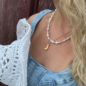 Close-up of double layer necklace with pearl strand and golden cowboy boot pendant